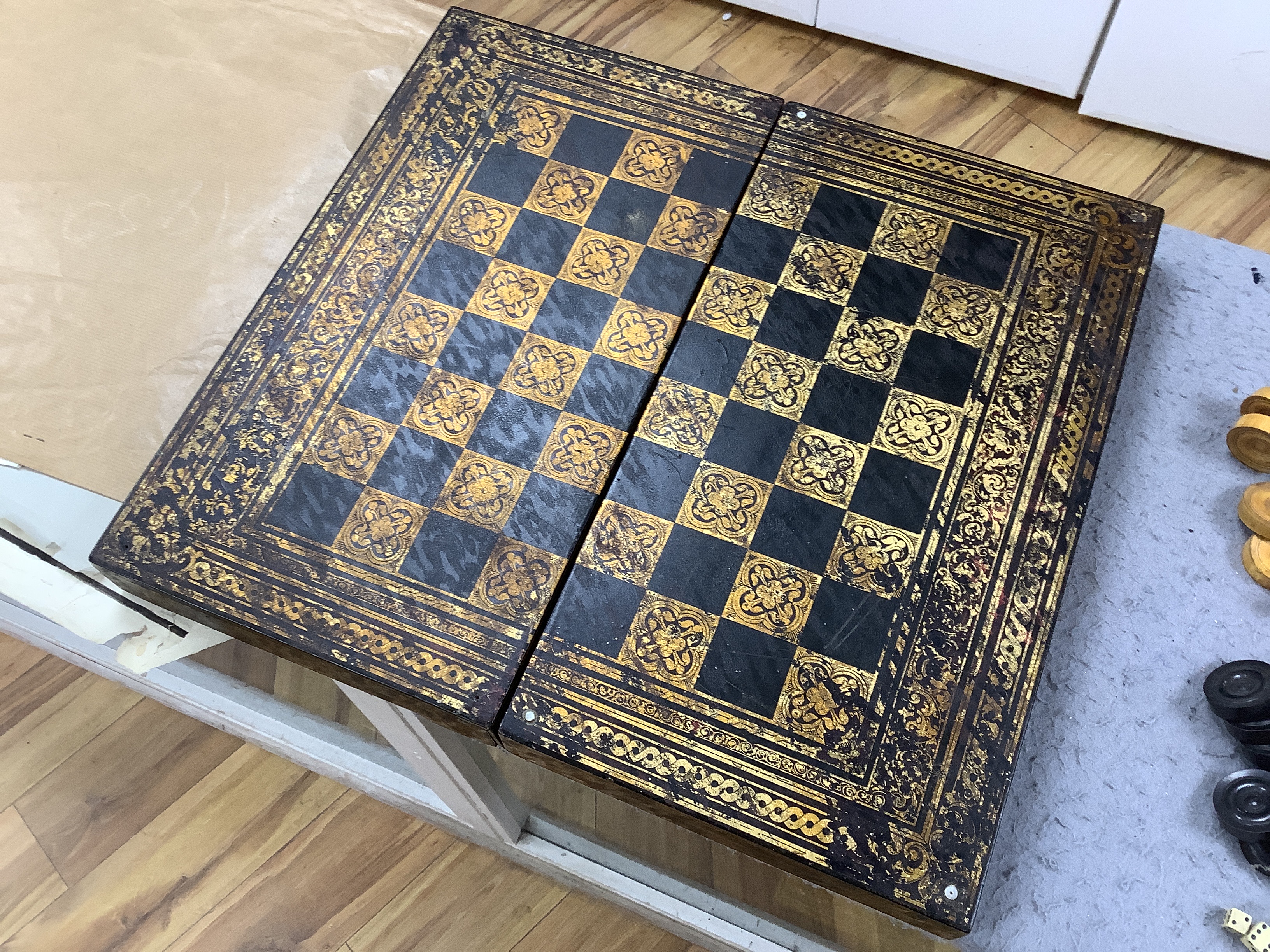 A 19th century papier maché folding games board for chess and backgammon, containing a wooden draughts set etc. with gilt decoration, 41 x 45cm unfolded